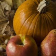 A flat lay of a pumpkin, a pomegranate, two pears and an apple on top of fall leaves