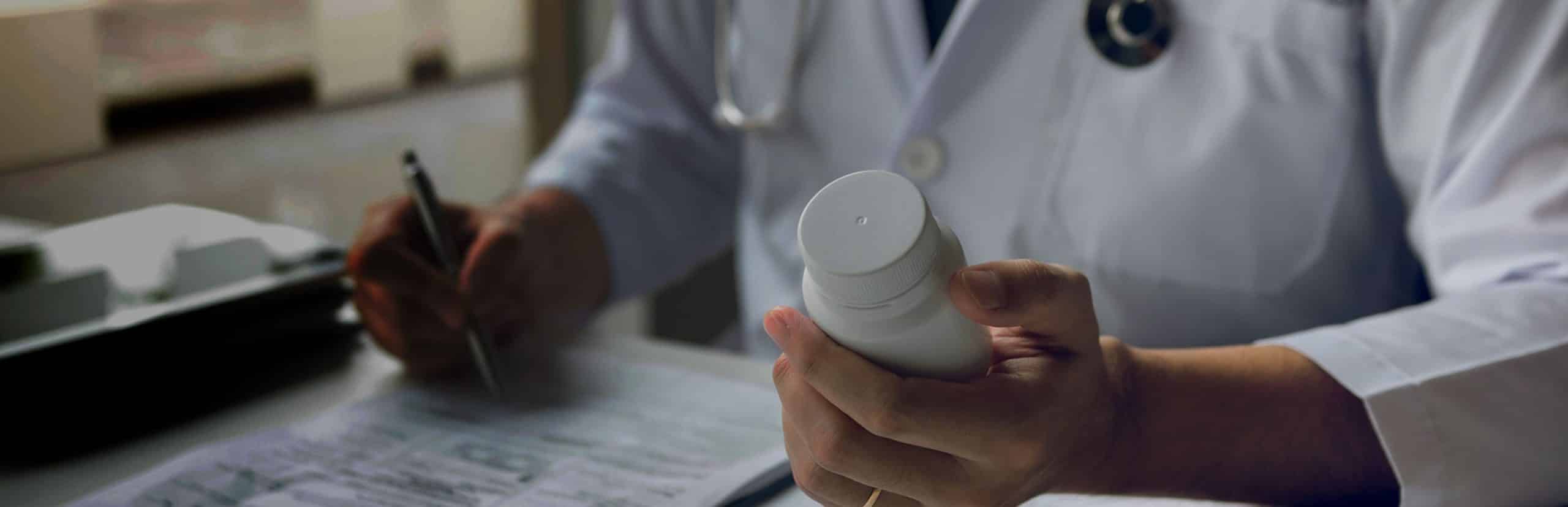 A doctor holding a bottle of medicine and writing a prescription