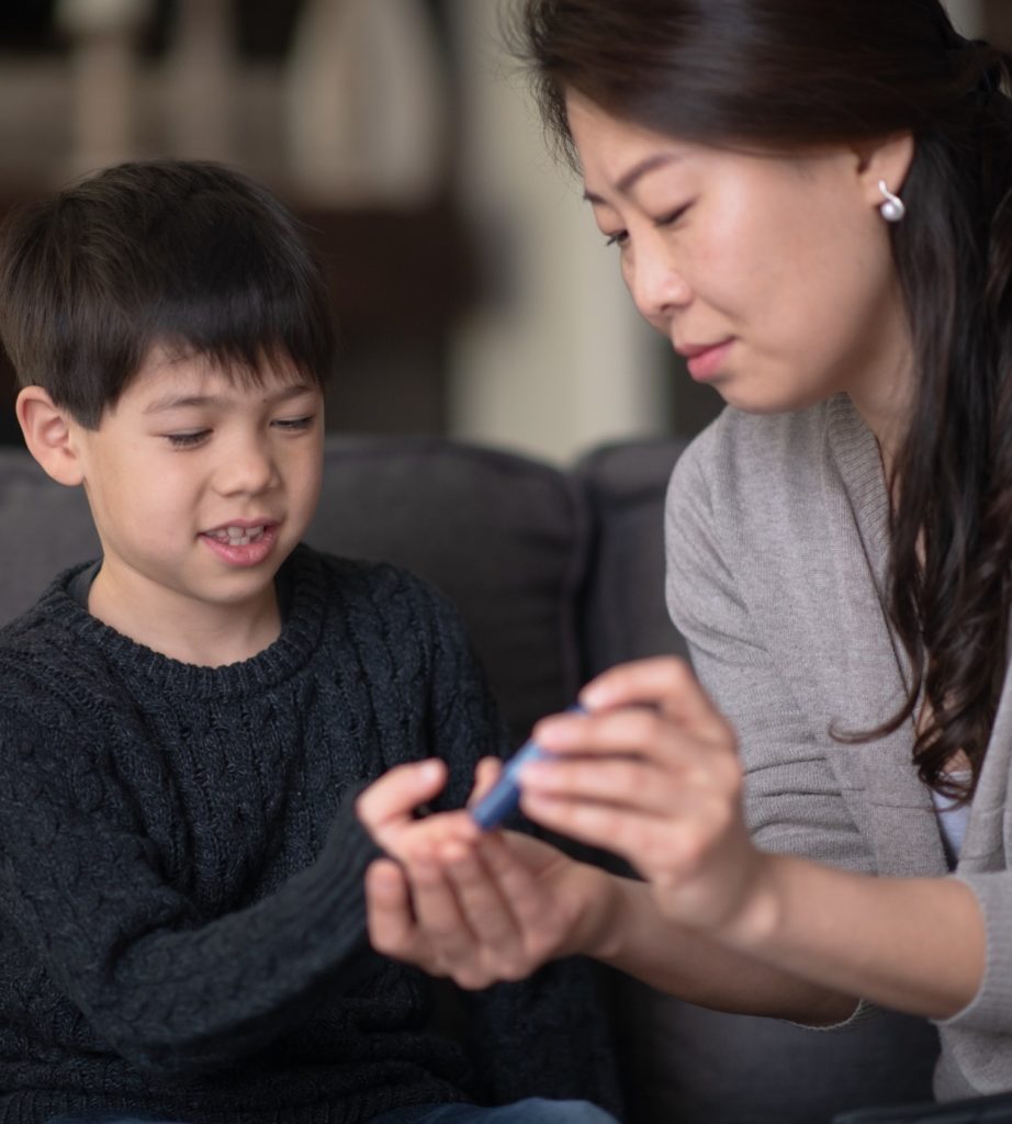 A mom and son sitting on a couch while she uses a lancet device to measure his glucose