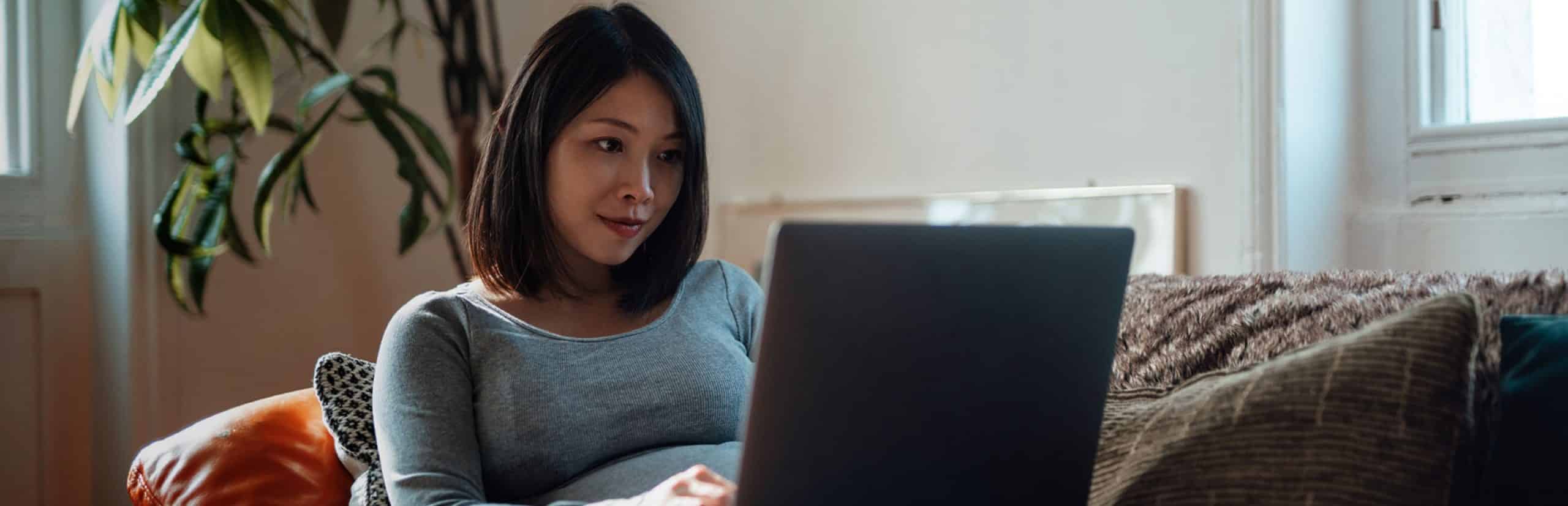 Pregnant woman sitting on her couch, looking at her computer