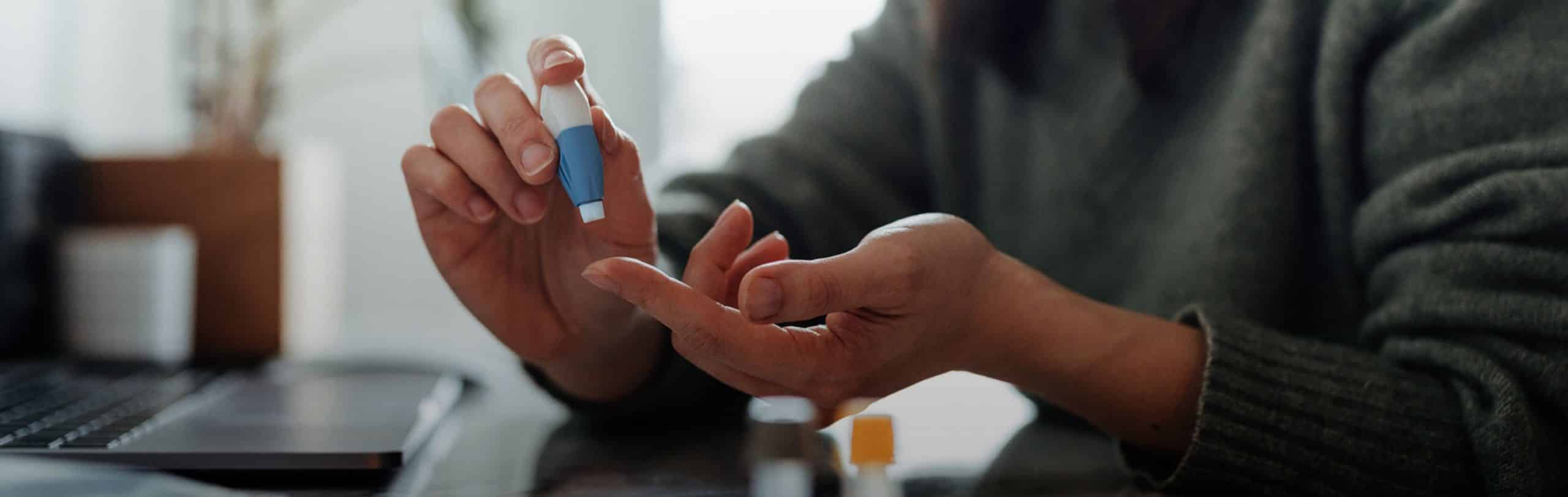 A close-up photo of a woman testing her glucose with a lancet device