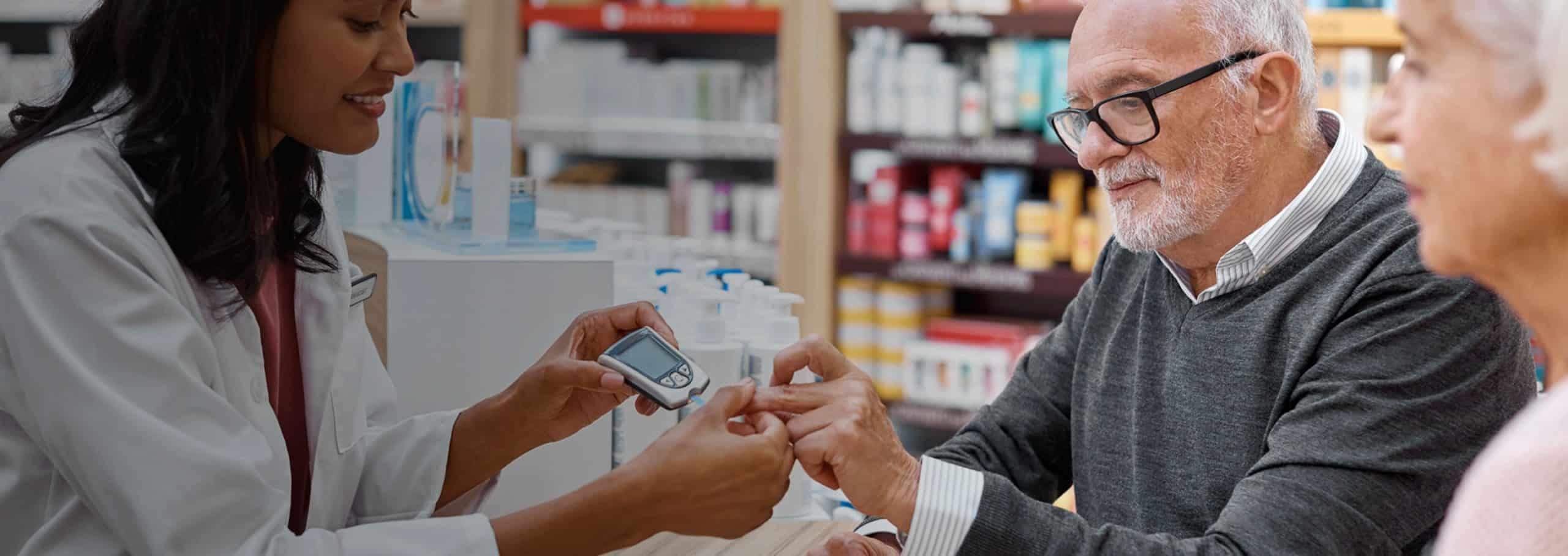 Female pharmacist showing an elderly male customer how to use a glucose meter