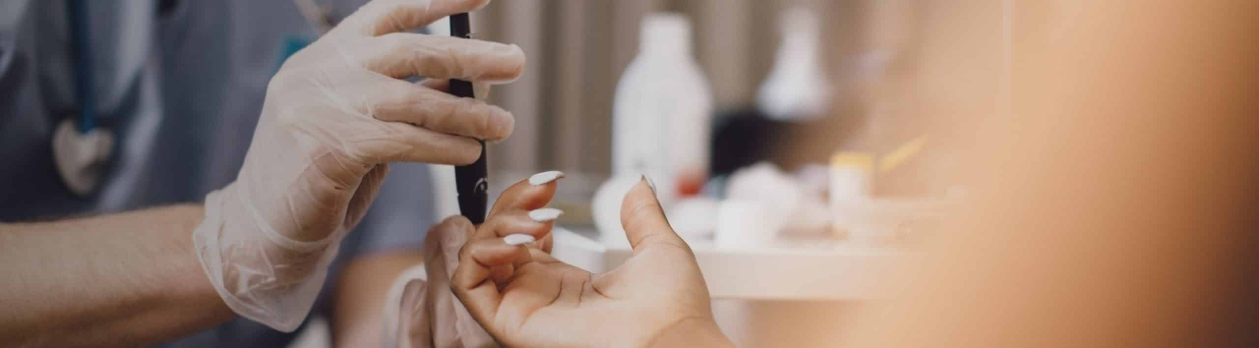 A closeup of a medical professional using a lancet device on a female patient's finger