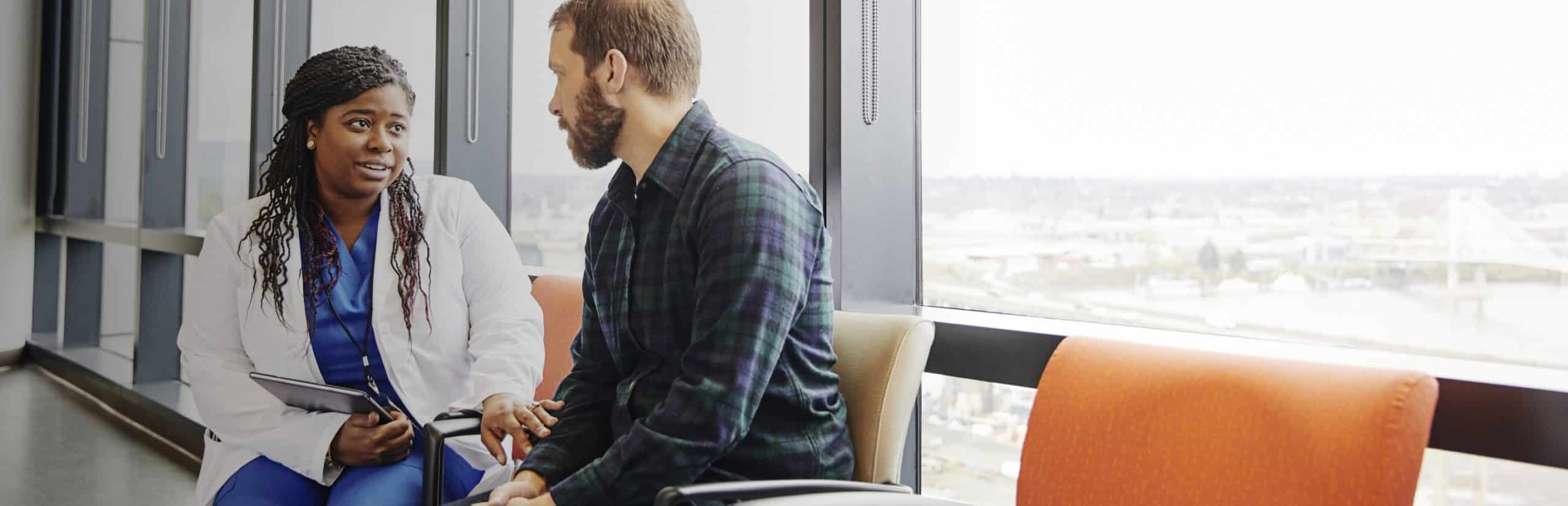 Female healthcare professional talking to a male patient while sitting in front of a window