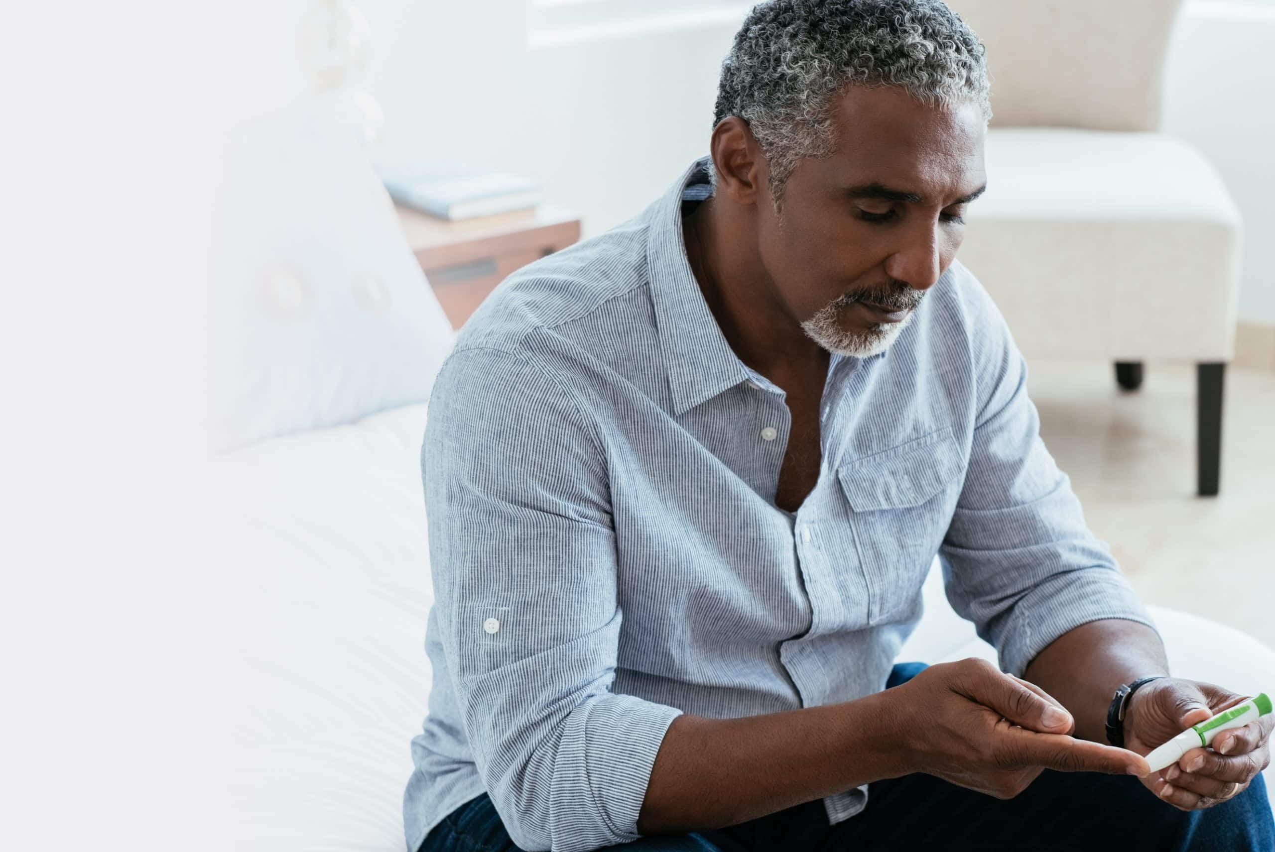 A man sitting on his bed, use a lancing device on his index finger