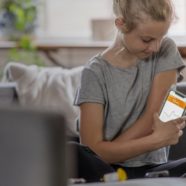 A young girl sitting on her couch, monitoring her glucose with a continuous glucose monitor