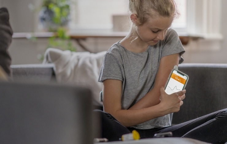 A young girl sitting on her couch, monitoring her glucose with a continuous glucose monitor