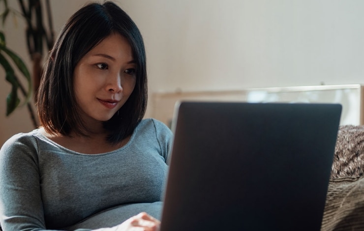 Pregnant woman sitting on her couch, looking at her computer