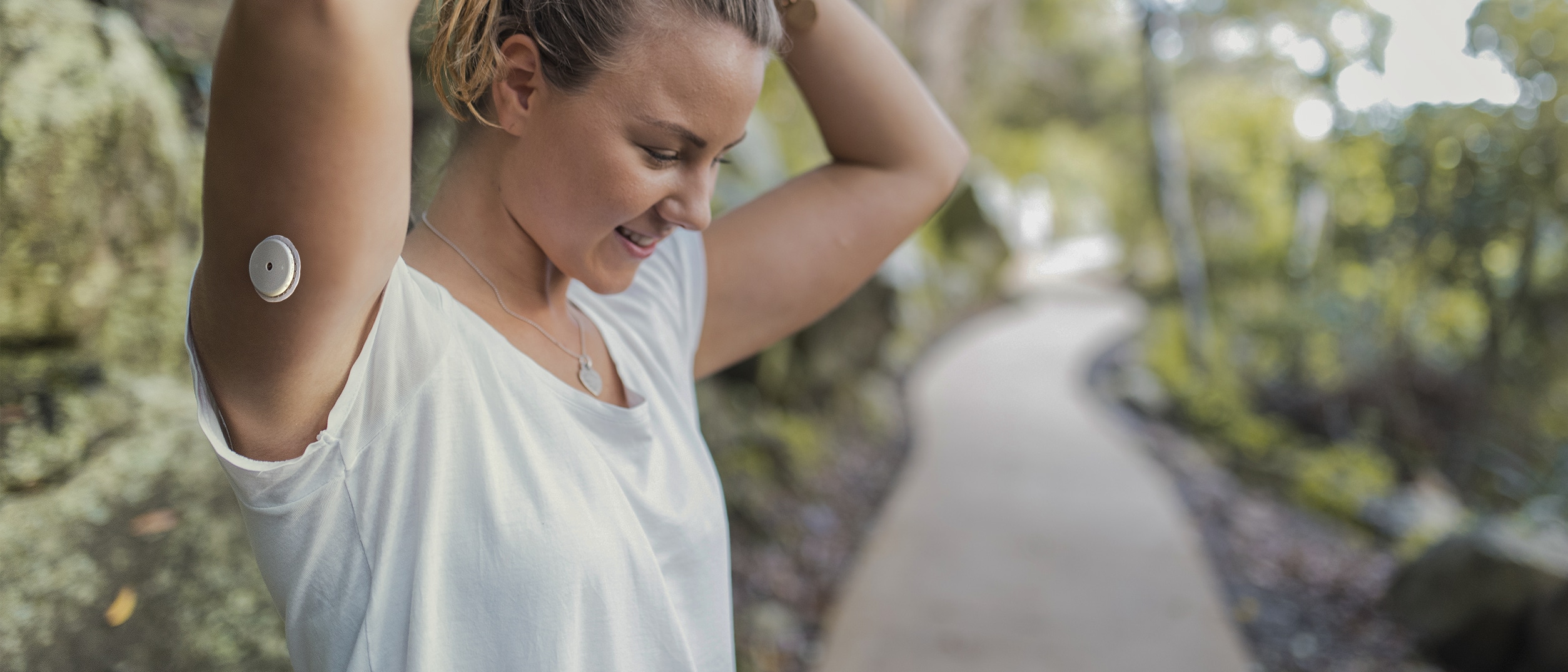 Woman wearing and insulin pump on her arm, tying her hair back in preparation for a run