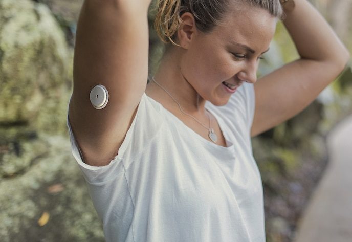 Woman wearing and insulin pump on her arm, tying her hair back in preparation for a run