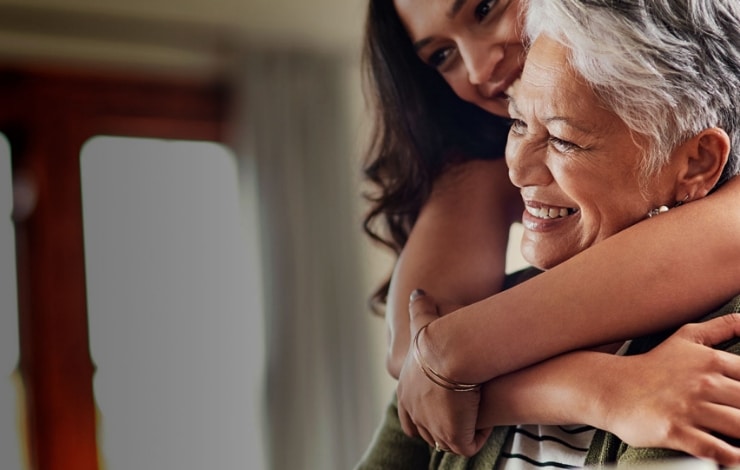 An elderly woman using her computer while her daughter hugs her from behind