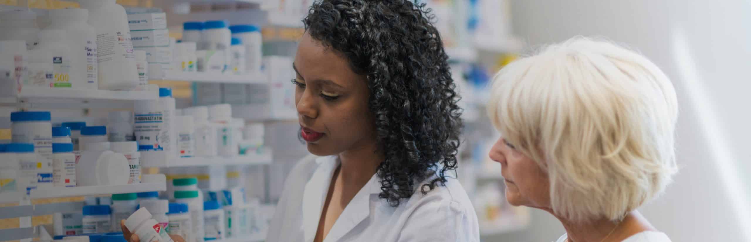 Female pharmacist helping a woman customer in front of a wall of medicine