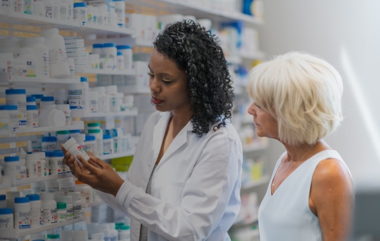 Female pharmacist helping a woman customer in front of a wall of medicine
