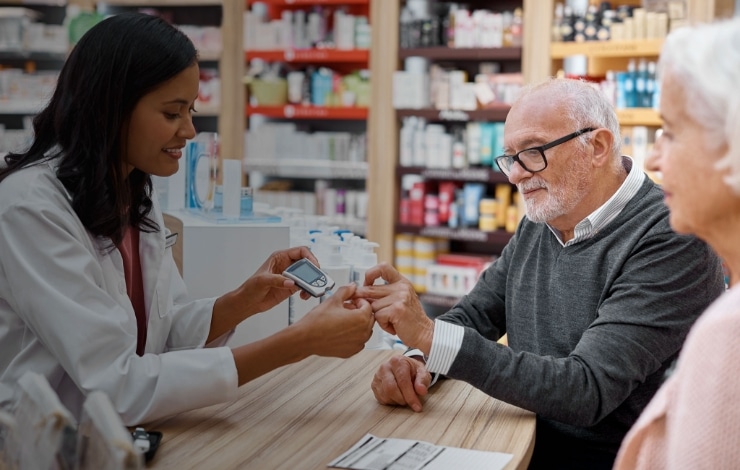 Female pharmacist showing an elderly male customer how to use a glucose meter