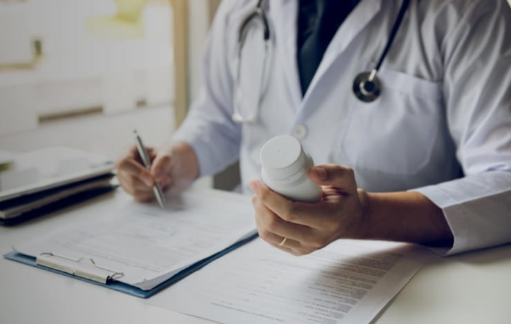 A doctor holding a bottle of medicine and writing a prescription