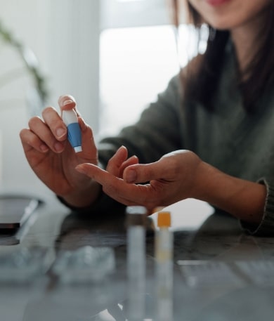 A close-up photo of a woman testing her glucose with a lancet device