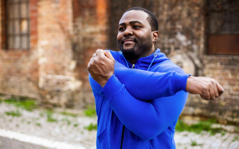 An African-American man in a blue hoodie is shown stretching his arm.