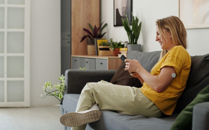 A woman wearing a CGM laughs while looking at her phone.